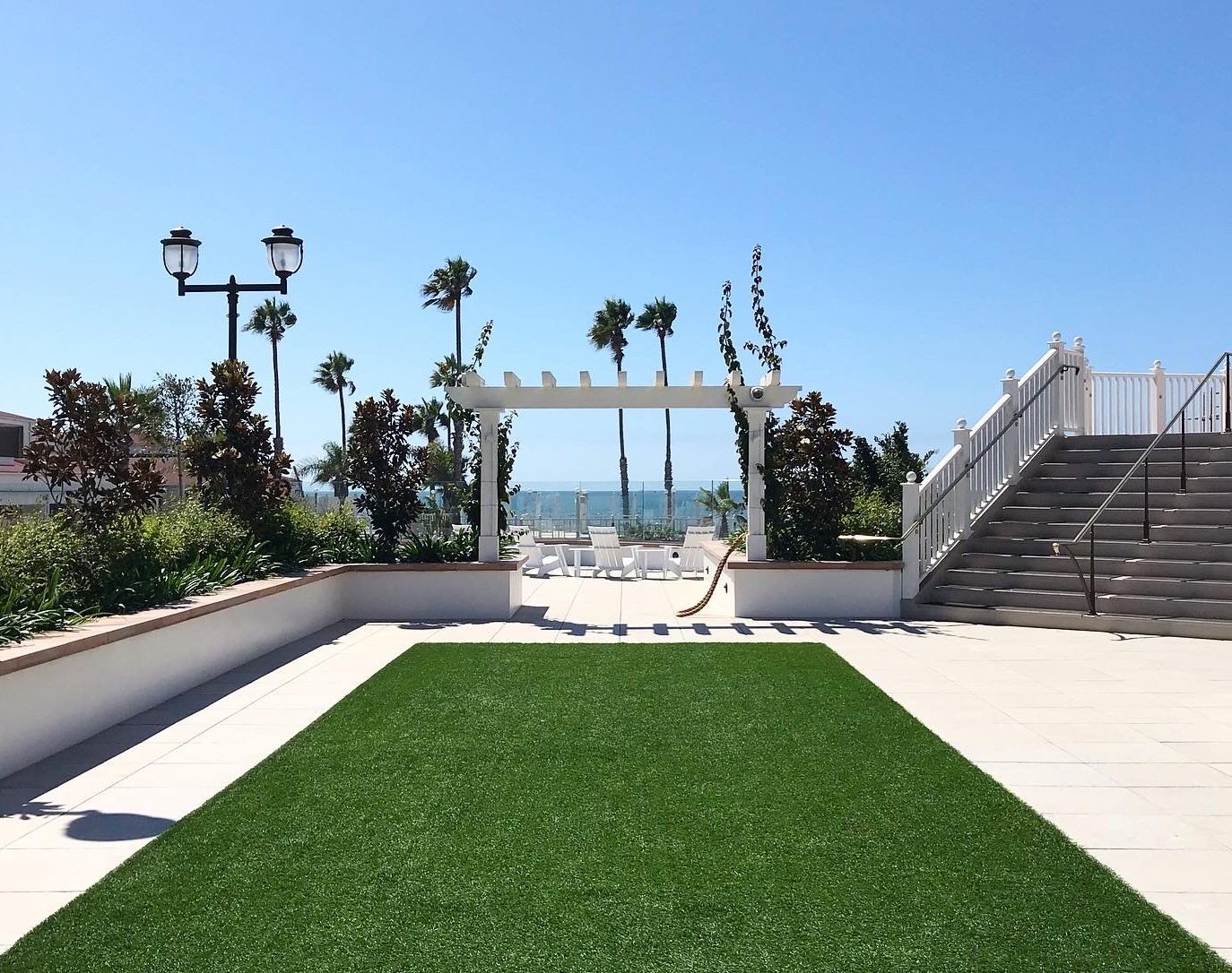 A photograph taken in Coronado, CA, of an empty plaza with green astro turf, lounge chairs, and ocean beach.