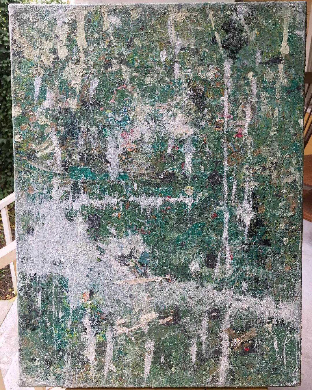 A painting of light green, red, black, white paint splatters created through chance and kinetics. Adhered with mod podge, newspaper, and magazine pages.